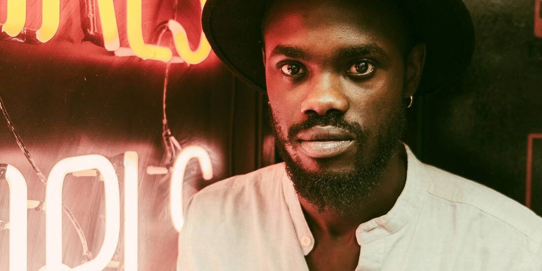 Man in a hat standing near a neon sign.