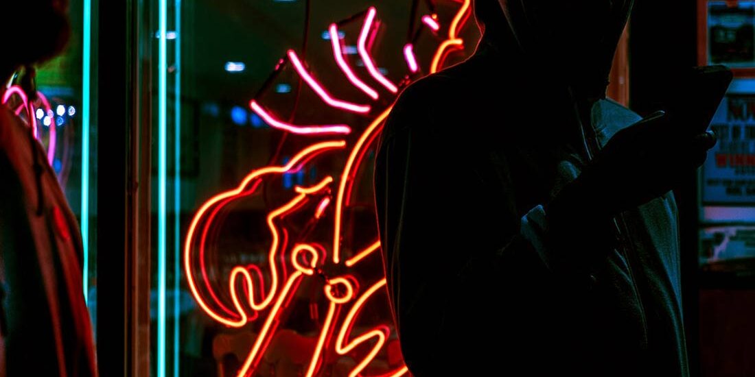 Two people silhouetted against a neon lobster sign at night.