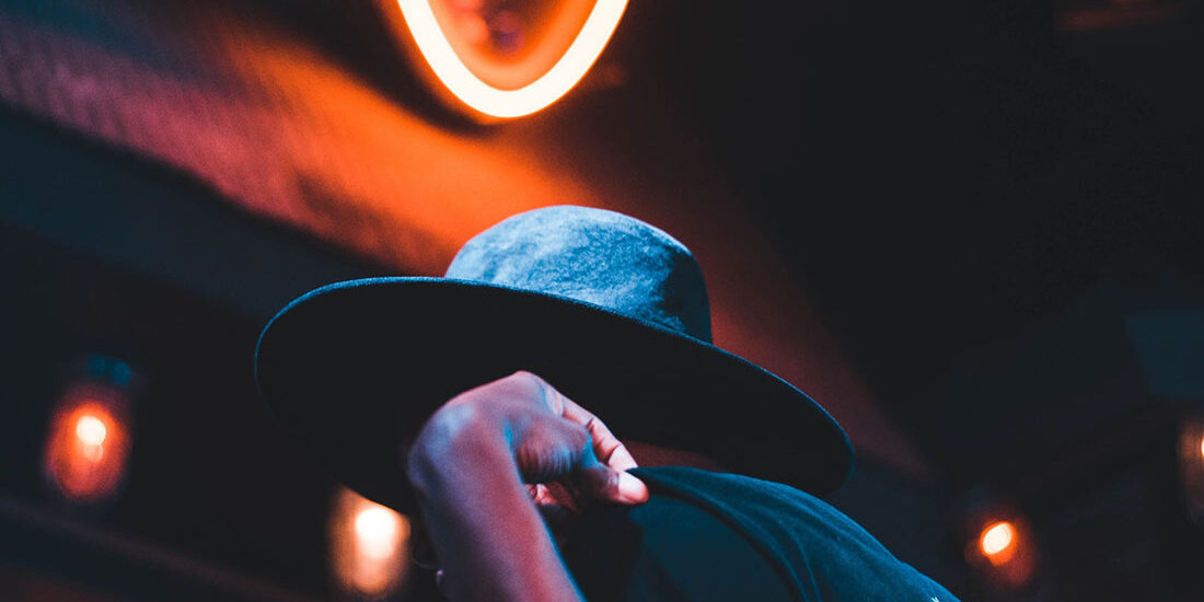 A person wearing a hat illuminated by neon lights in a dark setting.