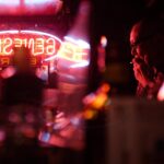 A person smoking near neon lights in a dark setting.