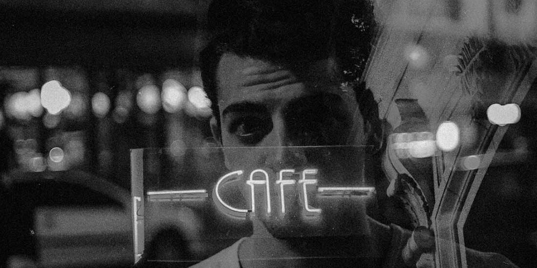 A man reflected in a glass window with the word 'CAFFE'.