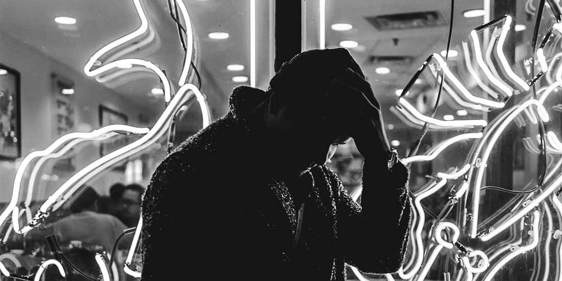 Silhouette of a person in front of bright neon fish signs.