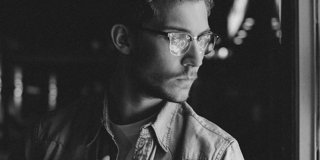 Black and white portrait of a man with glasses looking out a window.