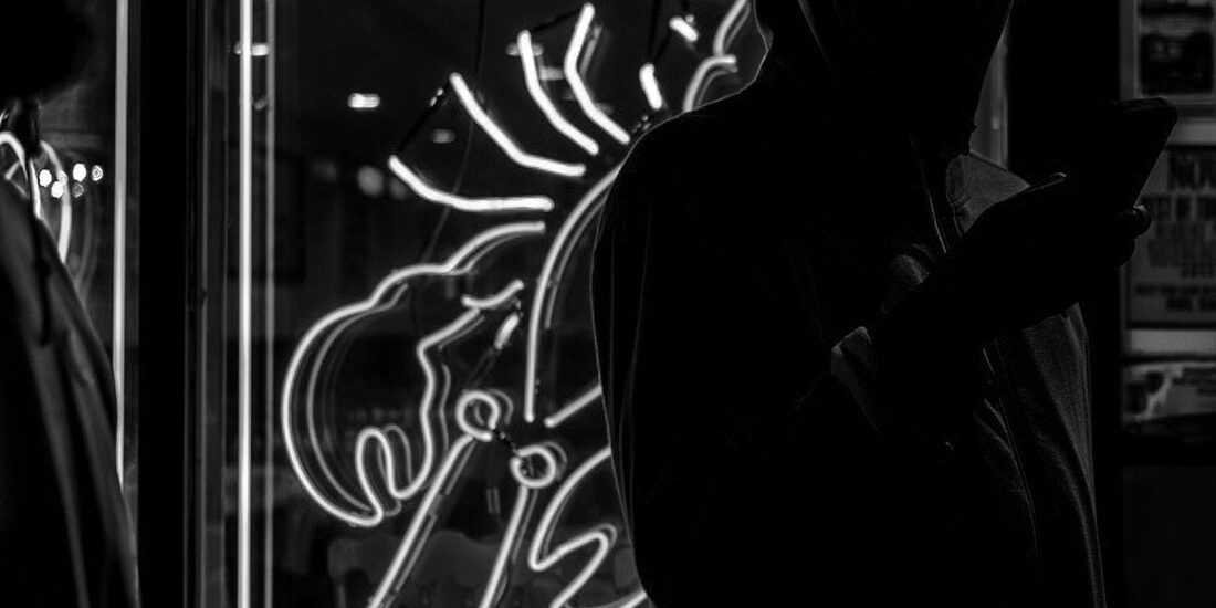 Silhouettes of two people near a neon scorpion sign at night.